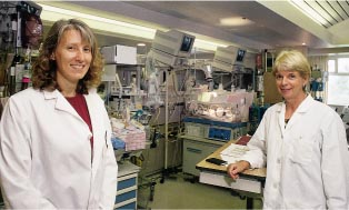 Two women in lab coats in front of acrylic bassinets