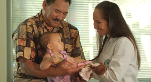 Winston Kong holds young Li`ulani Martin, being examined by Dr. Kapua Medeiros, JABSOM Class of 2010