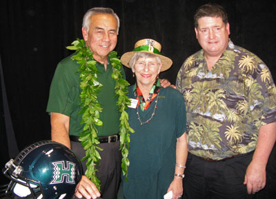 Norm Chow, Virginia Hinshaw and Jim Donvan standing by U H football helmet