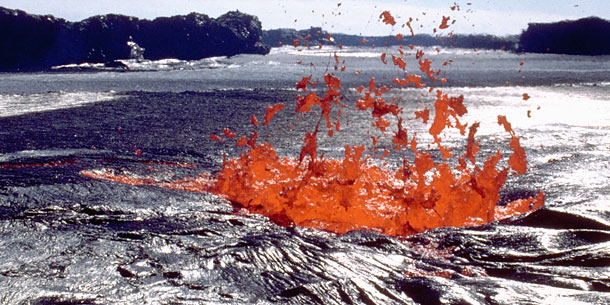 red molten lava spurting from opening in black lava field
