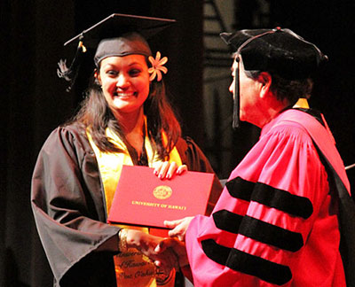 A student in cap and gown receiving diploma from chancellor