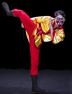 actor in bright red Monkey costume with mask in a one legged pose