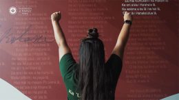 Back of a teacher with outstretched arms in front of a wall of Hawaiian language