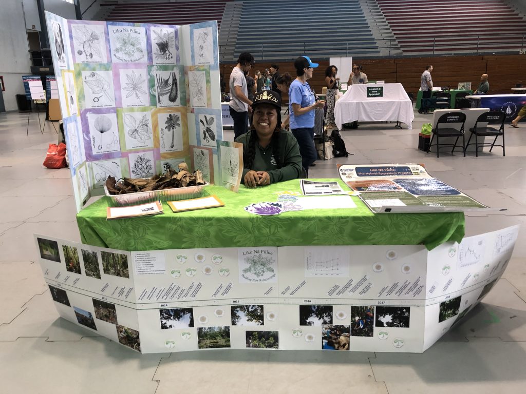 Young woman sits behind a table full of information about the plants and methods behind Liko Nā Pilina