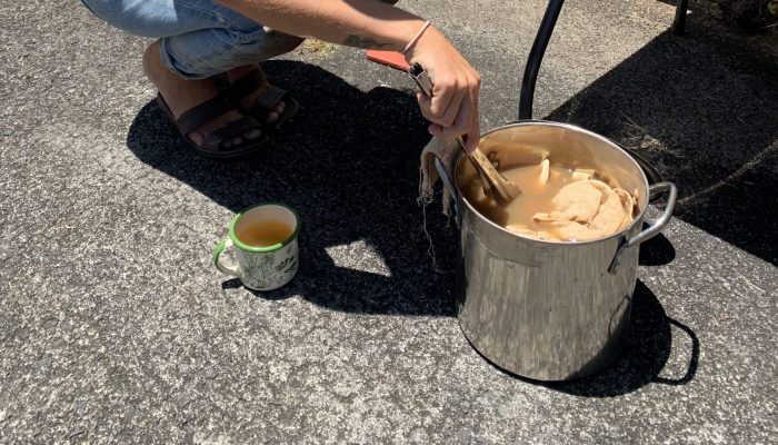 Young woman uses tongs to pull cloth out of a pot with orange-pink dye