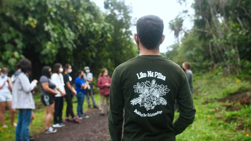 Man wearing Pilina shirt with his back to the camera, and a group of people in the background