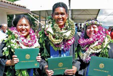 students in graduation regalia and lei, holding diplomas
