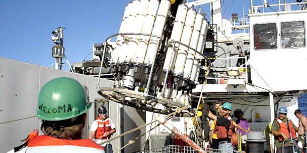 Men on board ship with array of white cylinders being lifted by hoist