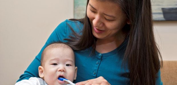 A woman brushing a babyʻs teeth
