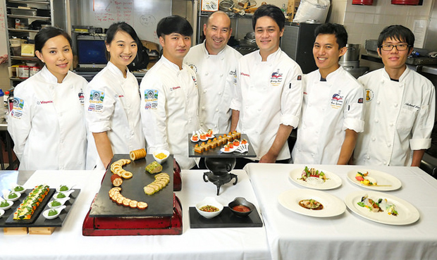 7 people wearing chef uniform standing behind culinary dishes