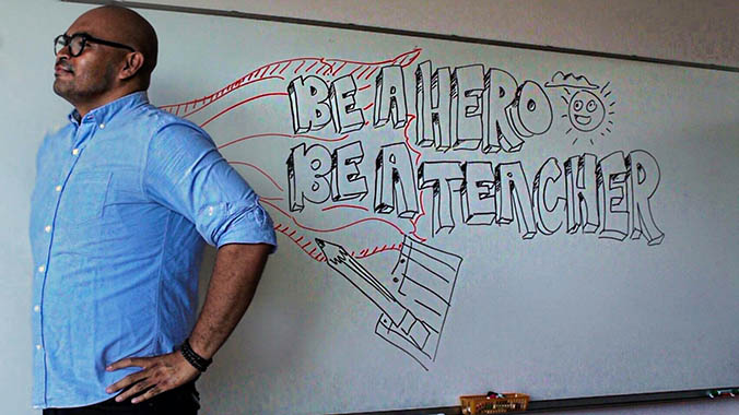 teacher in front of a whiteboard that says Be a Hero Be a Teacher