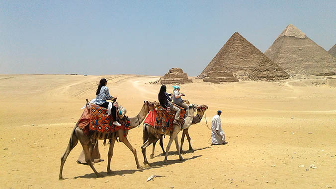 Students riding camels near the pyramids