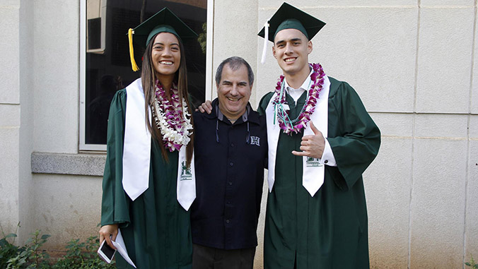Two student athletes in commencement regalia with David Matlin
