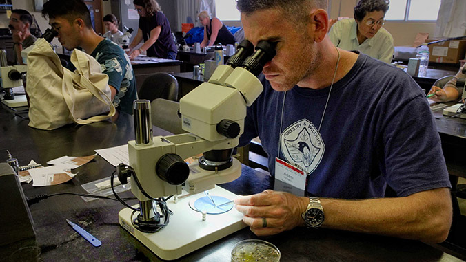 A man in a lab looking through a microscope