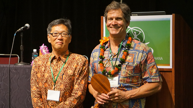 two people standing next to each other, one holding an award