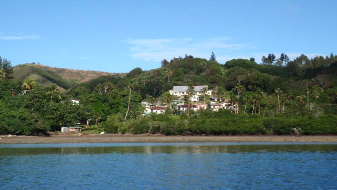 village surrounded by trees with ocean in front of it
