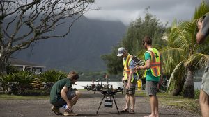 Three people standing around a landed drone, click for larger image