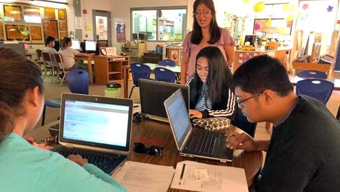 students looking at computer sitting a a table