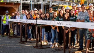 large group of people smiling and standing behind the signed steel beam