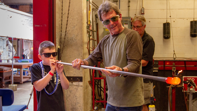 boy blowing in metal tube with hot glass on the end