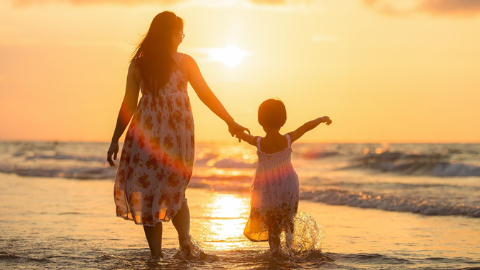 Backs of mother and daughter on the beach.