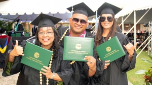 students in graduation regalia holding diploma