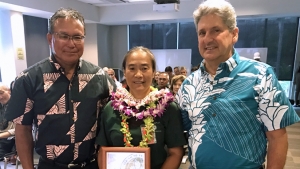 three people, one holding award and wearing lei