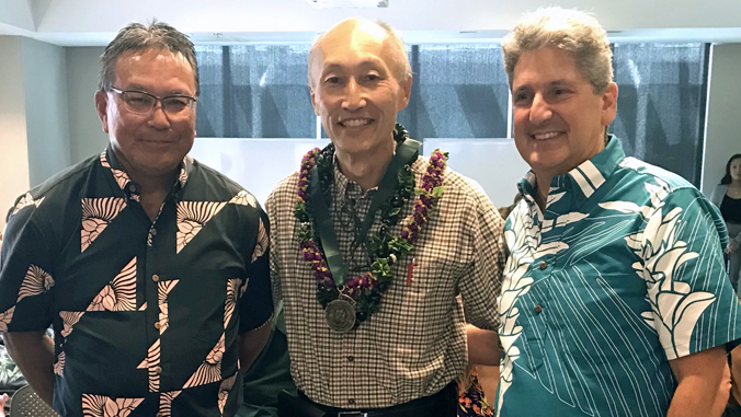 three people, one holding award and wearing lei