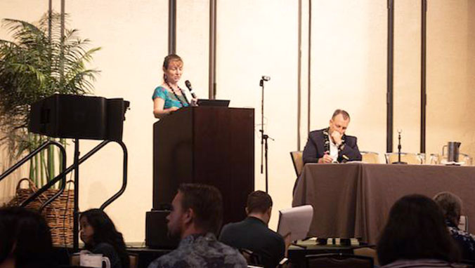 Woman at the podium and man sitting at table