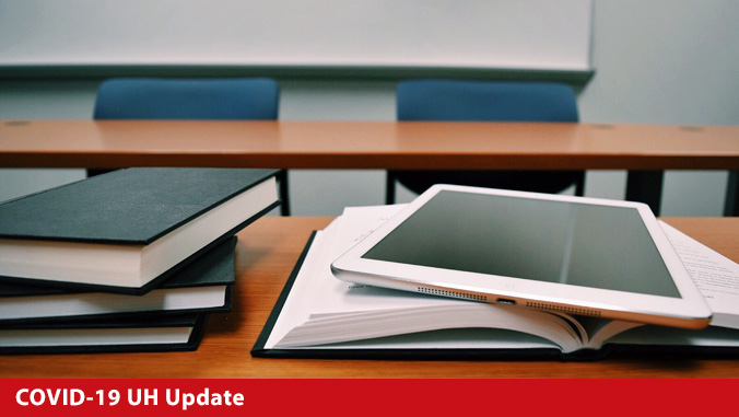 Tablet and books on desk with COVID-19 UH Update as text