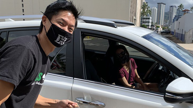 male staff with mask posing next to student in car