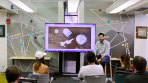person in front of screen speaking to group of people