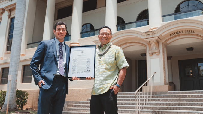 two people holding a certificate and standing in front of a building