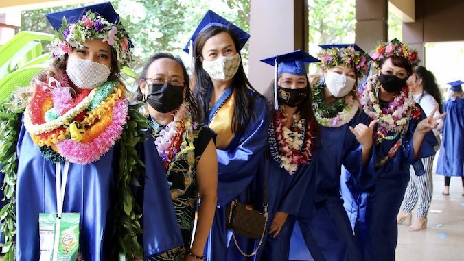 graduates with blue gown wearing lei and masks