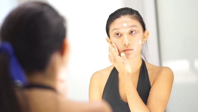 female applying sunscreen looking at mirror