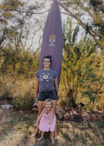 adult and child standing in front of a surfboard