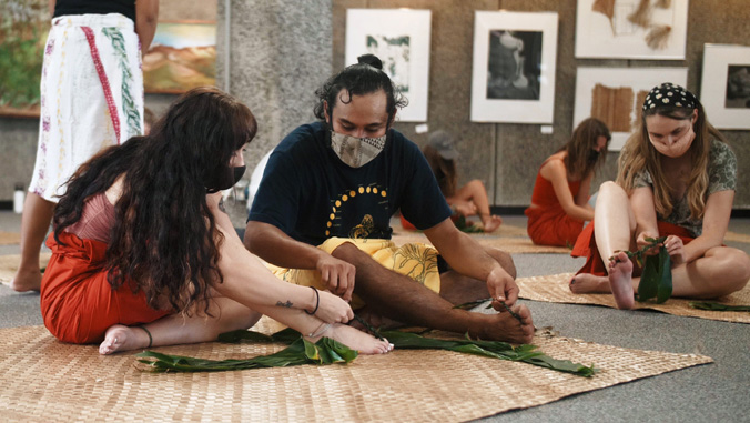 Two people seated with ti leaves