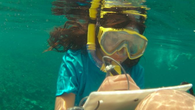 person with goggles writing on a pad underwater