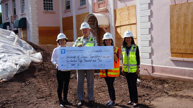 four people standing with hard hats and a large check