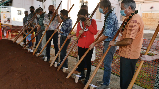 several people turning dirt with wooden poles