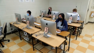 four people with masks sitting in front of computers