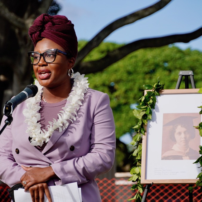 woman speaking at microphone, photo behind her