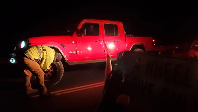Maunakea Rangers checking the tire of a red truck at night