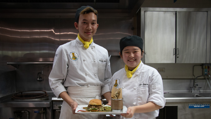 Two student chefs holding their dish of portobello burger and fries
