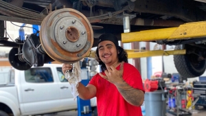 Student working under a car flashing a shaka