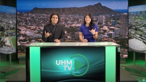 two people sitting on a green desk making a shaka sign