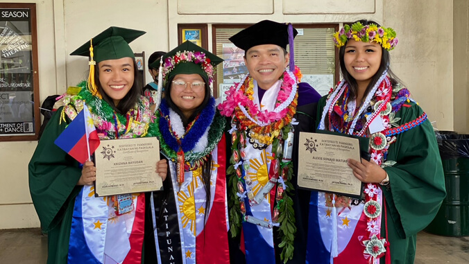 four people with graduation gowns smiling at the camera