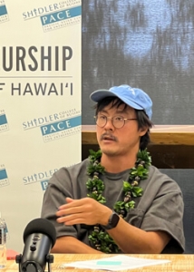 person with a hat and lei speaking into a microphone