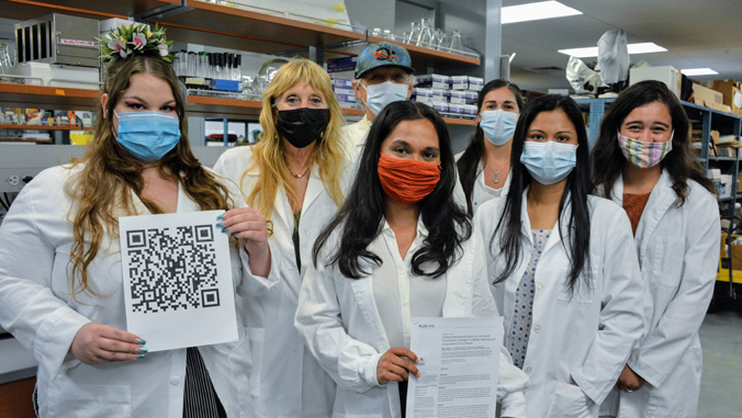 Researchers in a lab with a printed copy of their Plos One publication