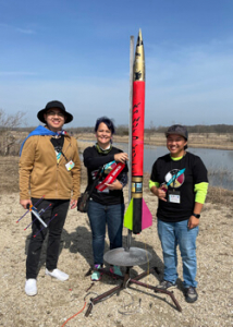 three people standing next to a rocket